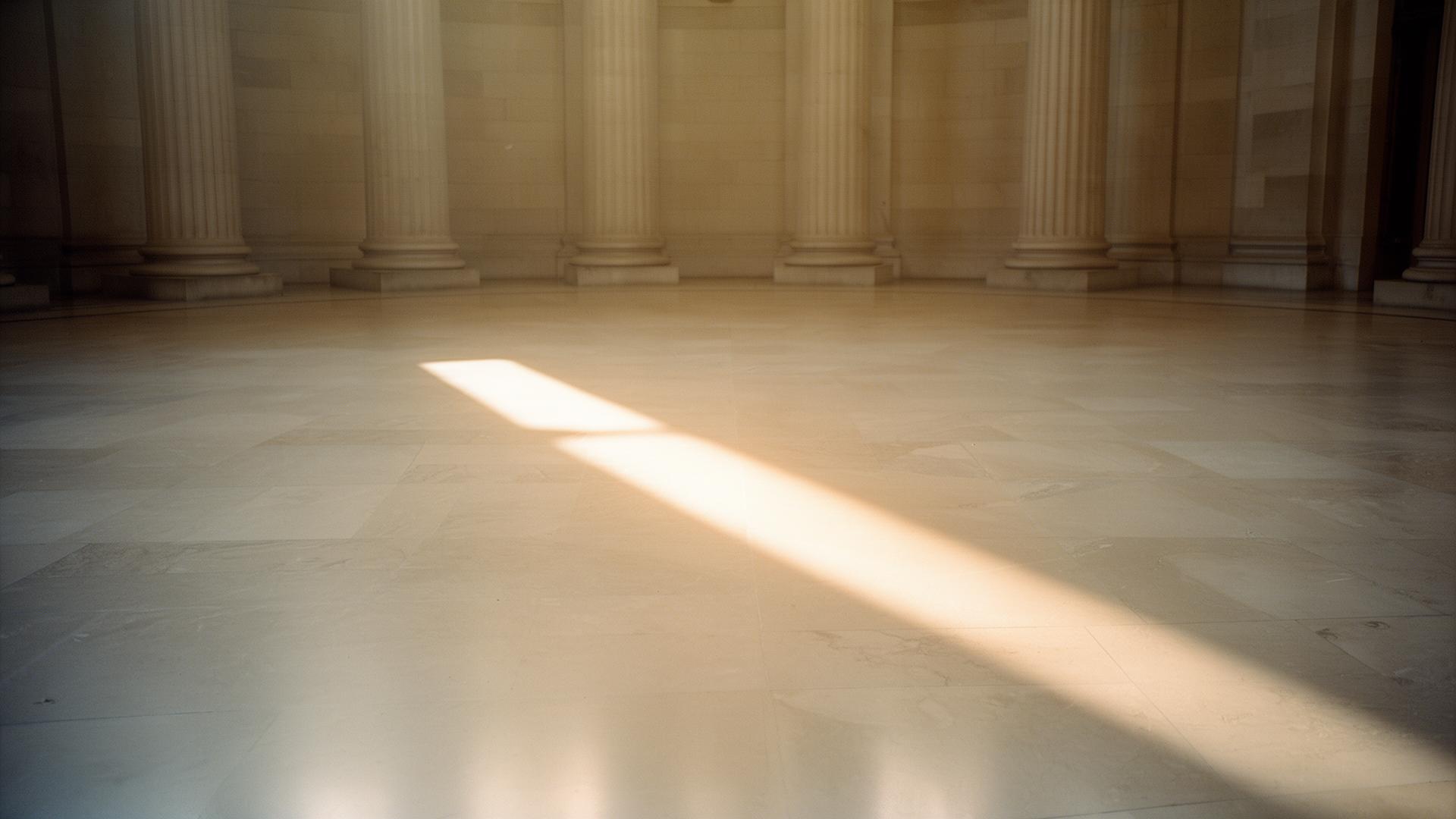 A single shaft of warm afternoon light across a polished limestone courthouse floor.
